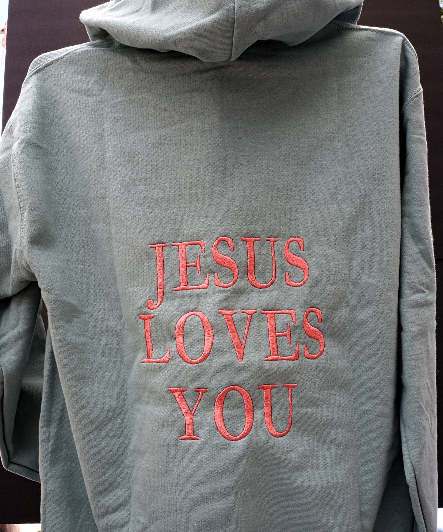 Jesus Loves You embroidered on the back of sage green hoodie