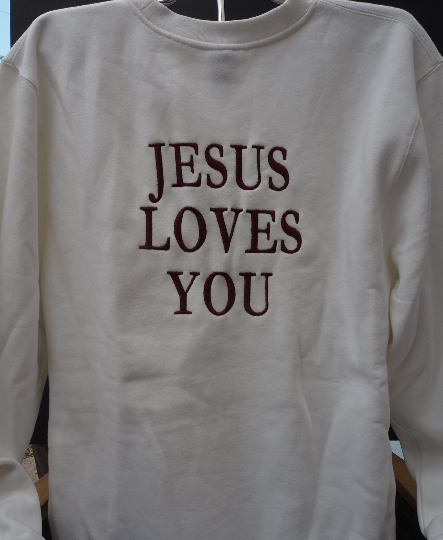 Jesus Loves You embroidered on the back of cream crewneck sweatshirt in burgundy